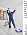 Worker dancing while holding paint roller on extension pole in bright room. Enjoying renovation process, positive mood during interior finishing and home improvement concept 143779157