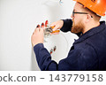 Electrician stripping wires with tool and preparing connections in wall sockets. Close up of electrical installation process, cable work and home renovation concept 143779158