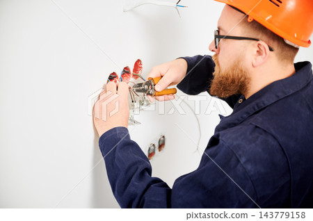 Electrician stripping wires with tool and preparing connections in wall sockets. Close up of electrical installation process, cable work and home renovation concept 143779158