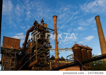High angle telephoto landscape of historic blast furnace complex with orange conical exhaust stack cowper stoves brick smokestack and blue sky in Duisburg Ruhr region North Rhine Westphalia Germany 143780266