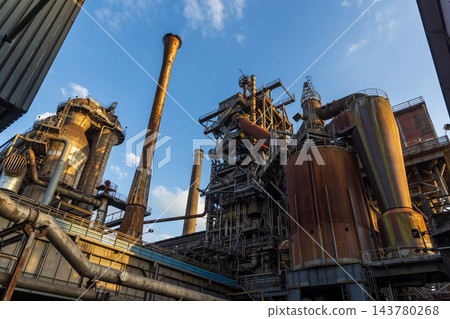 High angle telephoto landscape of historic blast furnace complex with dust collector cyclone orange conical exhaust stack cowper stoves and blue sky in Duisburg Ruhr region Westphalia Germany 143780268