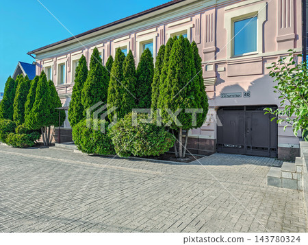 Facade of two-story house is decorated with green thuja trees Facade of two-story house is decorated with green thuja trees 143780324