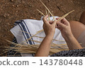 Hands of Senior Artisan Weaving Traditional Basket with Natural 143780448