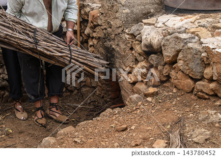 Man in Traditional Rustic Attire Carrying Firewood Bundle to an 143780452
