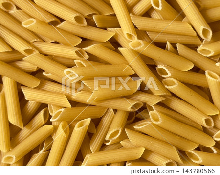 Raw penne pasta heap on a dark background. Dry uncooked penne pasta, textured background. Raw penne pasta heap on a dark background. Dry uncooked penne pasta, textured background. 143780566