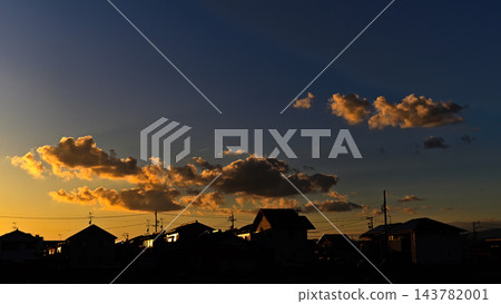 Clouds glowing golden in the setting sun, silhouetted against the backdrop of a residential area. Clouds glowing golden in the setting sun, silhouetted against the backdrop of a residential area. 143782001
