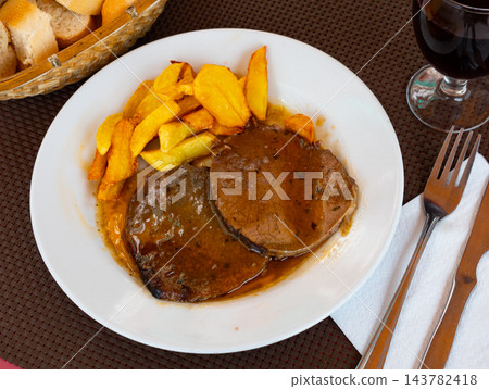 Tasty baked beef steak in fragrant gravy served with potatoes and pepper at plate. Traditional Spanish dish 143782418
