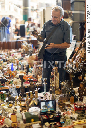 Elderly man is choosing vintage bronze vase at an outdoor flea market Elderly man is choosing vintage bronze vase at an outdoor flea market 143782491