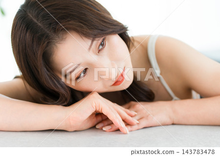 一位美麗的女子手托下巴,雙手交叉放在桌上。美容與化妝品 一位美麗的女子手托下巴,雙手交叉放在桌上。美容與化妝品 143783478