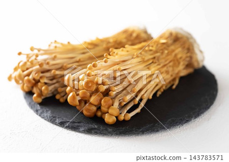 白色背景上的黑色盤子上擺放著棕色的金針菇。 白色背景上的黑色盤子上擺放著棕色的金針菇。 143783571