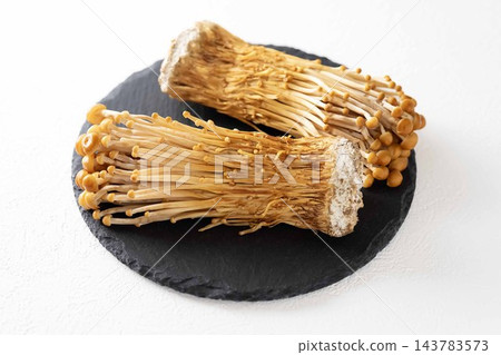 白色背景上的黑色盤子上擺放著棕色的金針菇。 白色背景上的黑色盤子上擺放著棕色的金針菇。 143783573