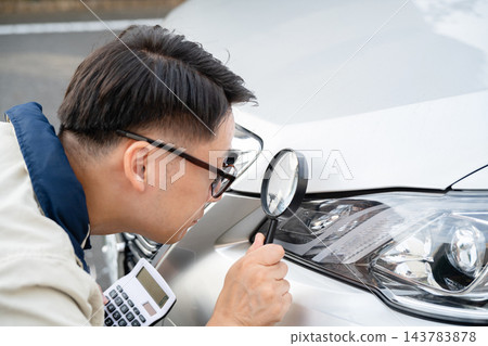一名男子正在檢查他汽車的損壞情況。 一名男子正在檢查他汽車的損壞情況。 143783878