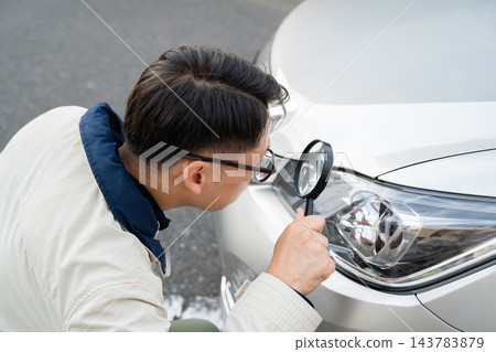 一名男子正在檢查他汽車的損壞情況。 143783879