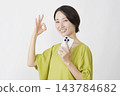 一位中年婦女在白色背景下舉著智慧型手機，比出「OK」手勢。 143784682