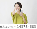一位中年婦女在白色背景前豎起大拇指，同時舉起她的智慧型手機。 143784683