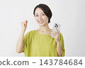 一位中年婦女在白色背景前舉著智慧型手機，做出勝利的手勢。 143784684