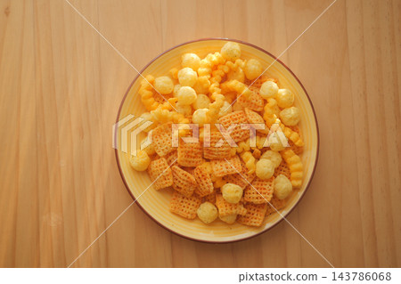Bowl of cheese crackers and puffed snacks on a wooden table Bowl of cheese crackers and puffed snacks on a wooden table 143786068