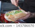 Cook adds sauce to a filled sandwich during food preparation 143786070