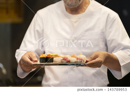 壽司師傅手捧盛在方形盤子裡的壽司。 壽司師傅手捧盛在方形盤子裡的壽司。 143789953