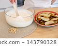 Baker occupation. Mixing dough. Female hand stirring flour batter at home kitchen counter preparing dessert with sliced pear pine nuts. 143790328