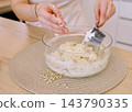 Kneading dough. Culinary work. Female baker hand adding flour mixing ingredient in glass bowl preparing healthy cookies with pine nuts. 143790335