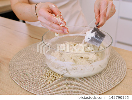Kneading dough. Culinary work. Female baker hand adding flour mixing ingredient in glass bowl preparing healthy cookies with pine nuts. 143790335