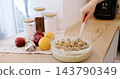 Kitchen work. Homemade treat. Female baker hand stirring wet dough with chopped nut on table with bright fresh fruit glass jar set. 143790349