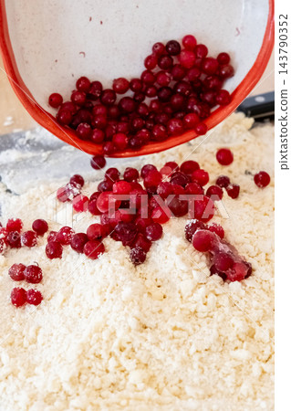 Berry pastry preparation. Baking cookies. Pouring red cranberry from bowl in flour crumbs pile making sweet treat with natural flavor. Berry pastry preparation. Baking cookies. Pouring red cranberry from bowl in flour crumbs pile making sweet treat with natural flavor. 143790352