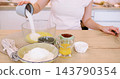 Home recipe. Dessert preparation. Baker female adding measured sugar egg to bowl with batter on table with baking ingredient dish. 143790354