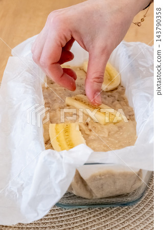 Cake making. Fruit pastry. Female confectioner hand adding pieces to dough in baking dish parchment on table cooking sweet banana bread. Cake making. Fruit pastry. Female confectioner hand adding pieces to dough in baking dish parchment on table cooking sweet banana bread. 143790358