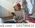 African American woman holding smartphone scrolling typing shopping online buying Christmas gifts. Girl buying on Internet chatting in social network enjoying Christmas winter holidays at home 143790410