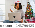 Merry Christmas. African woman in Santa hat having video chat in laptop. Blogger in festive mood recording video in social network. Girl having video call with friends family celebrating Christmas 143790425