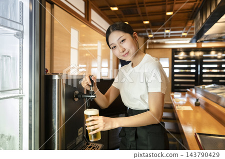 餐廳裡,一位年輕的女服務生正看著鏡頭,從服務生手中接過生啤酒倒出來。 餐廳裡,一位年輕的女服務生正看著鏡頭,從服務生手中接過生啤酒倒出來。 143790429