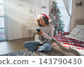 African American woman holding smartphone scrolling typing shopping online buying Christmas gifts. Girl buying on Internet chatting in social network enjoying Christmas winter holidays at home 143790430