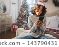 African American woman holding smartphone scrolling typing shopping online buying Christmas gifts. Girl buying on Internet chatting in social network enjoying Christmas winter holidays at home 143790431