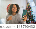 Merry Christmas. African woman in Santa hat having video chat in smartphone. Blogger in festive mood recording video in social network. Girl having video call with friends family celebrating Christmas 143790432