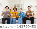 Home party. Cheerful group of friends playing video games at home. Happy diverse group buddies having fun together indoor. Friendship leisure entertainment concept. Young best friends enjoying weekend 143790453