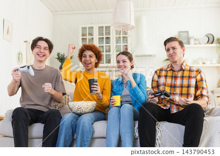 Home party. Cheerful group of friends playing video games at home. Happy diverse group buddies having fun together indoor. Friendship leisure entertainment concept. Young best friends enjoying weekend Home party. Cheerful group of friends playing video games at home. Happy diverse group buddies having fun together indoor. Friendship leisure entertainment concept. Young best friends enjoying weekend 143790453