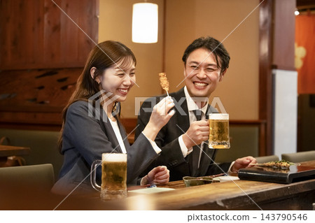 一男一女在吧台座位上享用烤雞串和啤酒。 一男一女在吧台座位上享用烤雞串和啤酒。 143790546