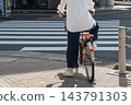 The back view of a young woman waiting at an intersection for a traffic light while straddling a bicycle. 143791303