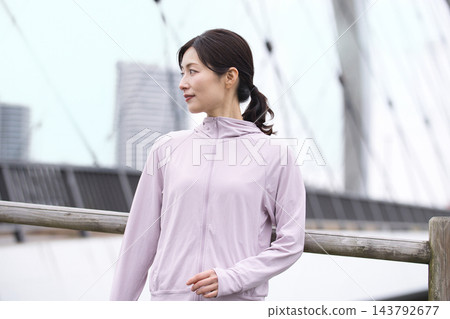 一位中年婦女身穿運動服沿著河岸行走。 一位中年婦女身穿運動服沿著河岸行走。 143792677