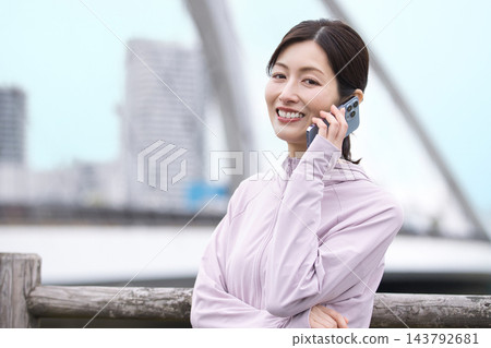 一位中年婦女身穿運動服,邊走邊用智慧型手機通話。 一位中年婦女身穿運動服,邊走邊用智慧型手機通話。 143792681
