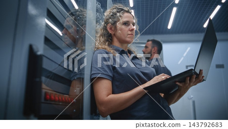Female Server Room Technician Analyzing Server Performance While Colleague Checks Other Racks 143792683