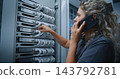 Female IT Specialist Consulting Colleague by Smartphone While Inspecting Server Cable Connections 143792781