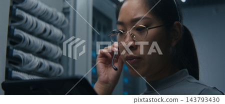 Female Network Engineer Using Tablet and Headset to Coordinate Technical Tasks Female Network Engineer Using Tablet and Headset to Coordinate Technical Tasks 143793430