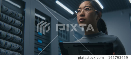 Young Female IT Specialist Reviews Technical Data on Tablet in Modern Server Room. Young Female IT Specialist Reviews Technical Data on Tablet in Modern Server Room. 143793439