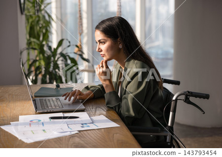 Focused businesswoman in wheelchair analyzing data on laptop 143793454