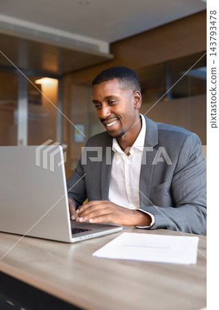 Black businessman sitting at office desk, working online using laptop Black businessman sitting at office desk, working online using laptop 143793478