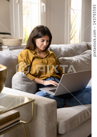 Woman focused on remote work using laptop on couch 143793593