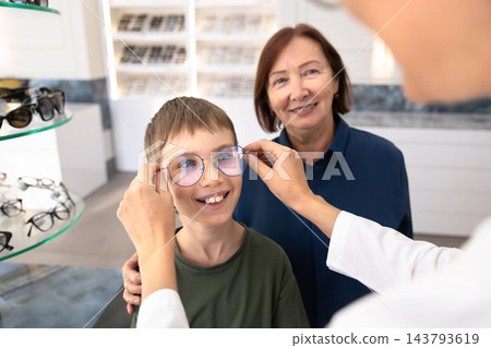 Female ophthalmologist putting new eyeglasses on child Female ophthalmologist putting new eyeglasses on child 143793619